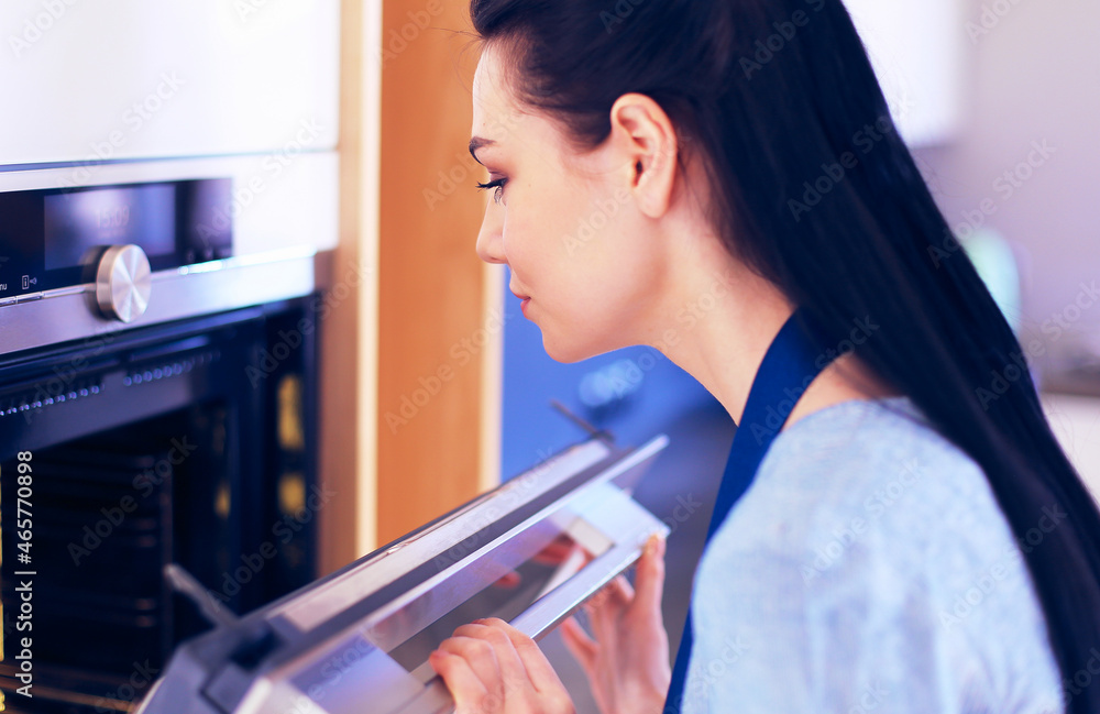 Beautiful young woman checking how her cake is doing in the oven Beautiful young woman checking how her cake is doing in the oven