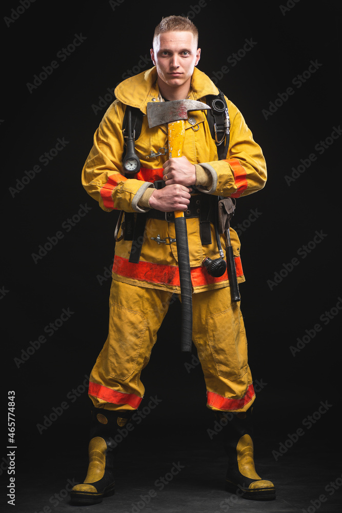 Firefighter holding helmet and jacket standing in studio against dark wall