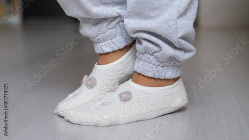 Legs of a woman in white socks walking on the wooden floor of her house with a sofa in the background. feet wearing white socks on gray wooden floor