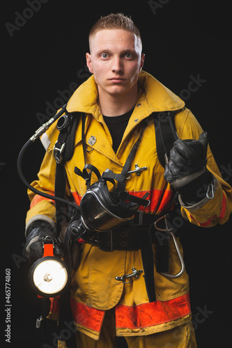 Firefighter holding helmet and jacket standing in studio against dark wall