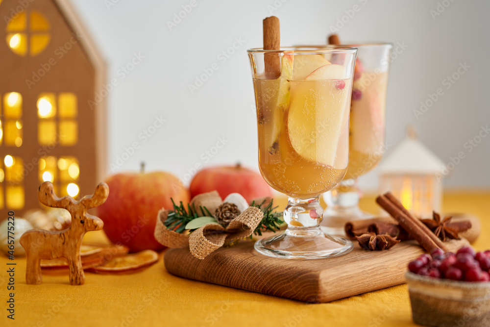 Two glasses of apple white mulled wine on wooden coaster. Christmas beverage with cinnamon, fruits and cranberry. Selective focus, blurred background, bokeh, horizontal, copy space