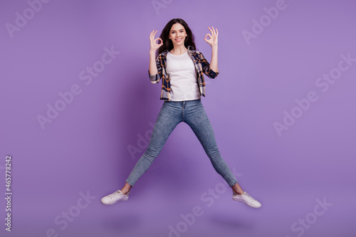Full size photo of young attractive girl happy positive smile jump up show okay alright sign isolated over violet color background