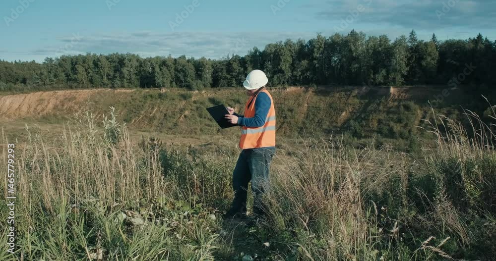 Working engineer in a white helmet next to a sand pit. The concept of mining, construction and industrial business. The foreman is talking on the phone discussing the workflow Working engineer in a white helmet next to a sand pit. The concept of mining, construction and industrial business. The foreman is talking on the phone discussing the workflow
