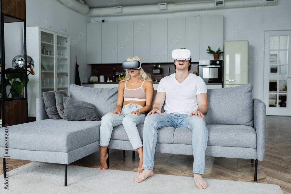 shocked couple in vr headsets sitting on grey couch shocked couple in vr headsets sitting on grey couch