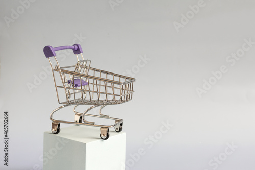 A blue empty metal shopping basket standing on a blue podium on a light background of kopi space. Shopping cart concept from stores