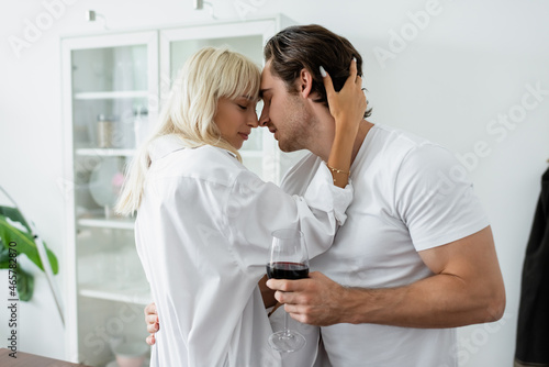 side view of young man with glass of wine hugging with blonde woman in modern kitchen