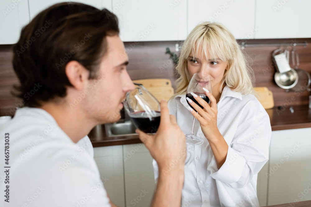 blonde woman drinking red wine and looking at blurred boyfriend blonde woman drinking red wine and looking at blurred boyfriend