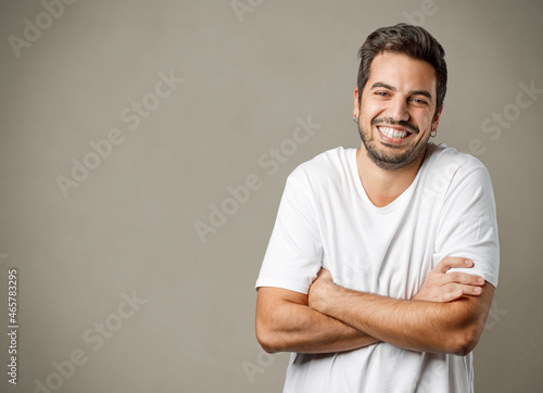 Portrait of handsome smiling man in white t-shirt with crossed arms isolated on gray brownish background. photo