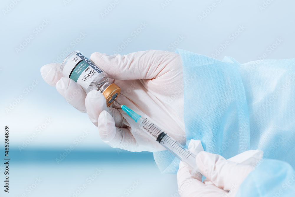 NO LOGOS OR TRADEMARKS! SELF MADE LABELS! Close up view of doctor’s hands with an ampule of covid vaccine and syringe on blue back NO LOGOS OR TRADEMARKS! SELF MADE LABELS! Close up view of doctor’s hands with an ampule of covid vaccine and syringe on blue back
