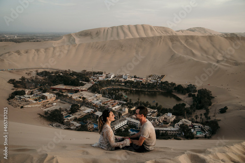 couple sitting in the dunes of Peru with oasis below