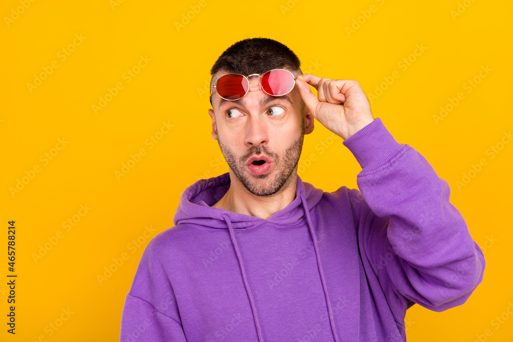 Photo of impressed millennial brunet guy look empty space wear eyewear purple hoodie isolated on yellow color background Photo of impressed millennial brunet guy look empty space wear eyewear purple hoodie isolated on yellow color background