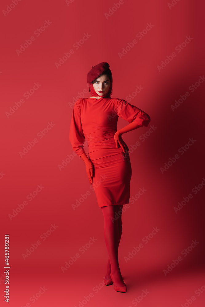 full length of young brunette woman in beret posing with hand on hip on red. full length of young brunette woman in beret posing with hand on hip on red.