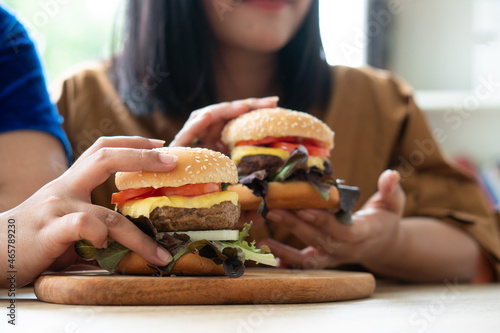 Hungry overweight woman holding hamburger on a wooden plate, During work from home, gain weight problem. Concept of binge eating disorder (BED).