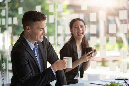 Friendly male leader laughing at group business meeting, happy young businesswoman enjoying fun conversation with partner, smiling business coach executive talking to colleague