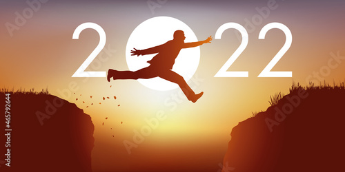 Un homme saute par dessus un gouffre entre deux falaises devant un soleil au zénith et symbolise le passage à la nouvelle année 2022.