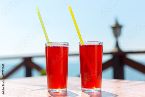 Two glasses with berry juice and strawberries on table of a street cafe against the background of the sea.
