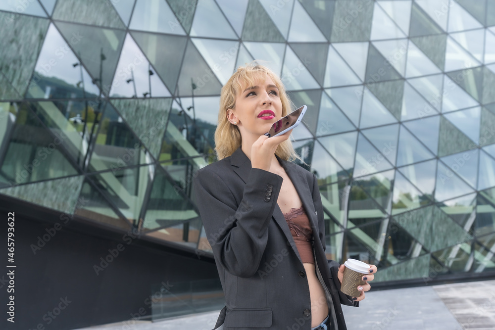 Entrepreneurial girl business park in a modern building with colored glass, young blonde woman in suit sending a voice note Entrepreneurial girl business park in a modern building with colored glass, young blonde woman in suit sending a voice note