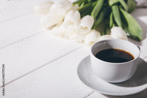 cup of coffee and white tulips on a wooden background.