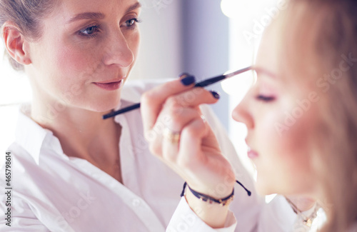 Young beautiful bride applying wedding make-up by professional make-up artist