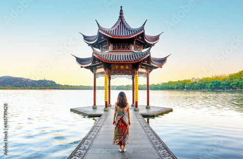 Beautiful scenery at Hangzhou West Lake, beautiful and elegant woman in dress looks on into the Jixian Pavilion and the vast lake at sunrise, Chinese characters translate as ‘Jixian Pavilion'