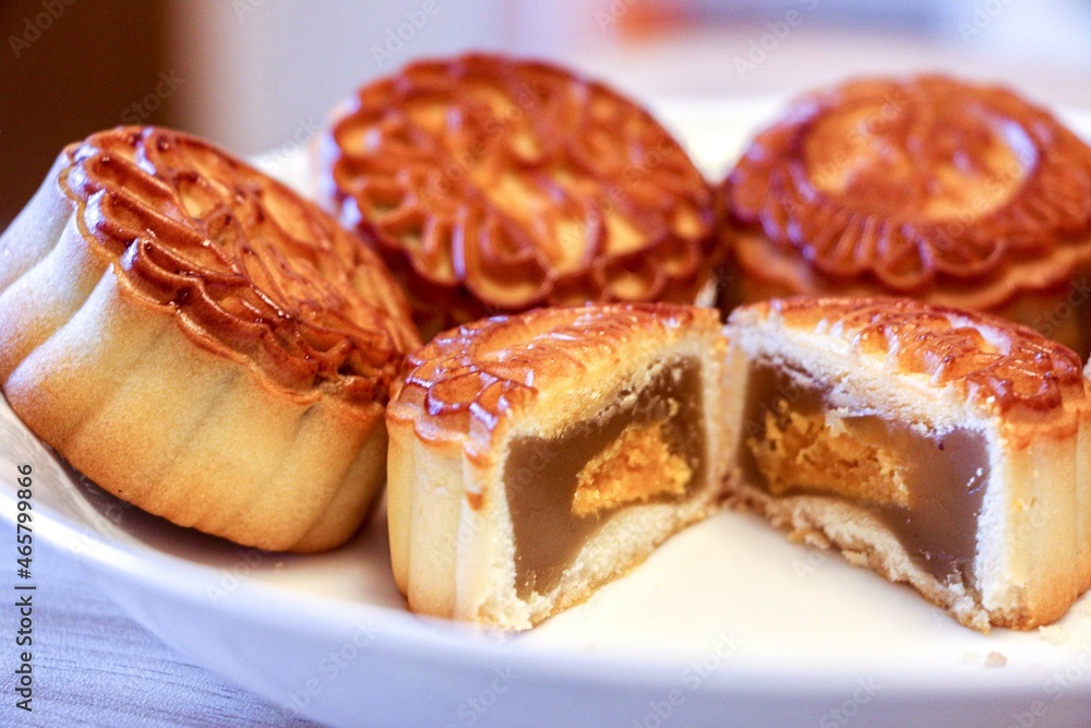 Close up of traditional delicious mooncake pastry cake cut open in half in the foreground showing sweet lotus seed paste and egg yolk filling. Full mooncakes in background.