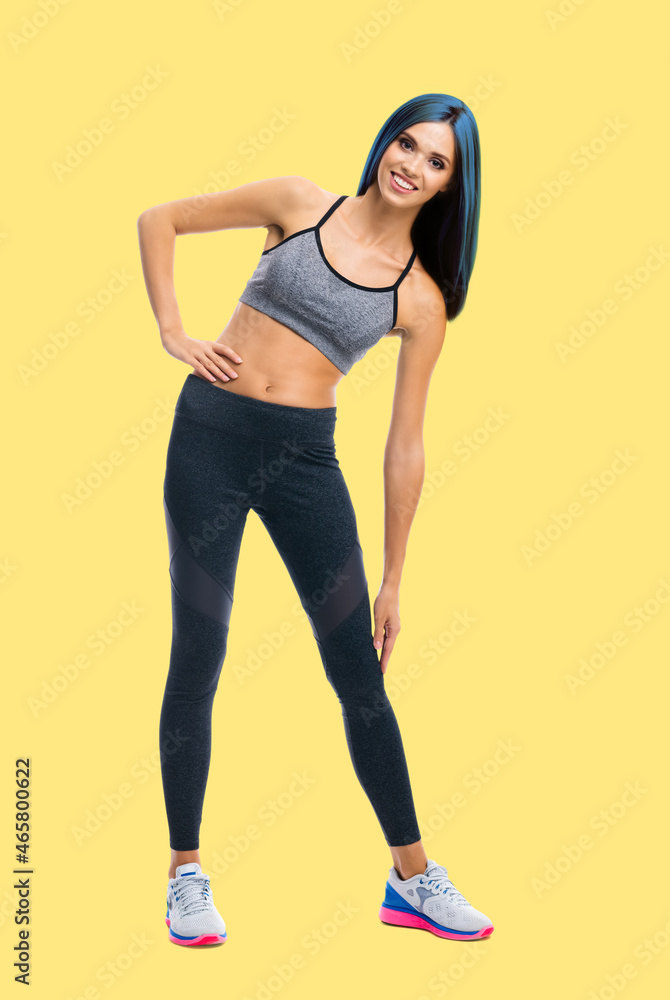 Full body portrait image of young happy smiling bright vivid blue haired slim woman doing fitness stretching exercise, isolated over yellow color background. Full body portrait image of young happy smiling bright vivid blue haired slim woman doing fitness stretching exercise, isolated over yellow color background.