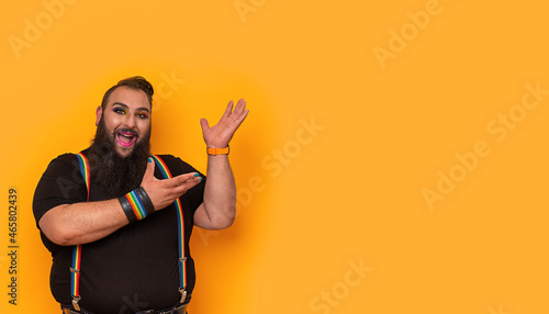 Happy bearded gay big man with rainbow trouser holder pointing side-up