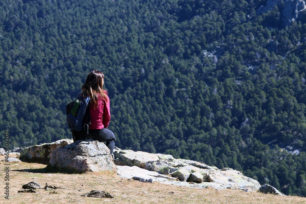 Naklejka premium Mujer joven descansando después de una subida de hiking admirando los pinares de la montaña. mirador de los Canchos en la Sierra de Guadarrama en Madrid, España.