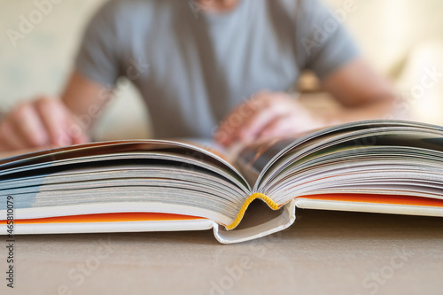 Close-up view of open book lying on table and man sitting in blurred background