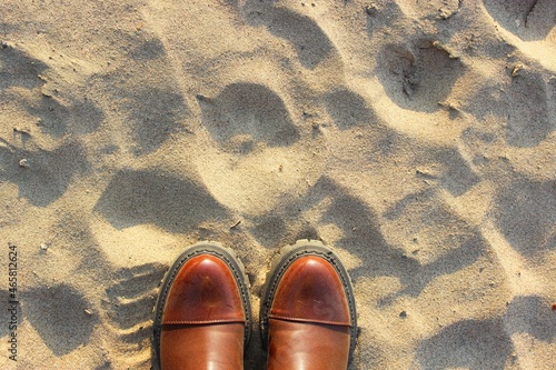 Female or male feet in shoes close-up and standing on the sand, top view. around yellow sand on the beach. brown leather boots with patent toe and black sole. place for text. to walk on the beach