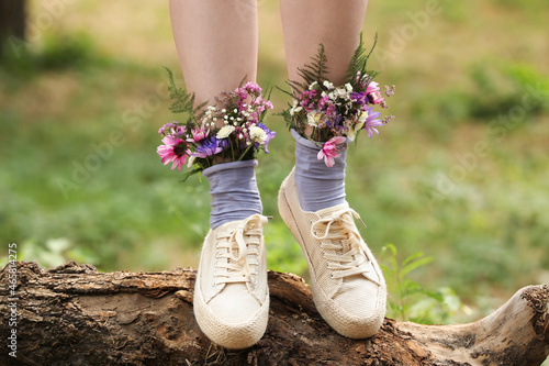 Woman standing on log with flowers in socks outdoors, closeup photo