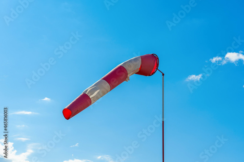 A torn red and white wind sock on a blue sky with clouds at an abandoned airfield