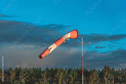 Red and white wind indicator in the shape of a cone at the airfield. Forest in the background