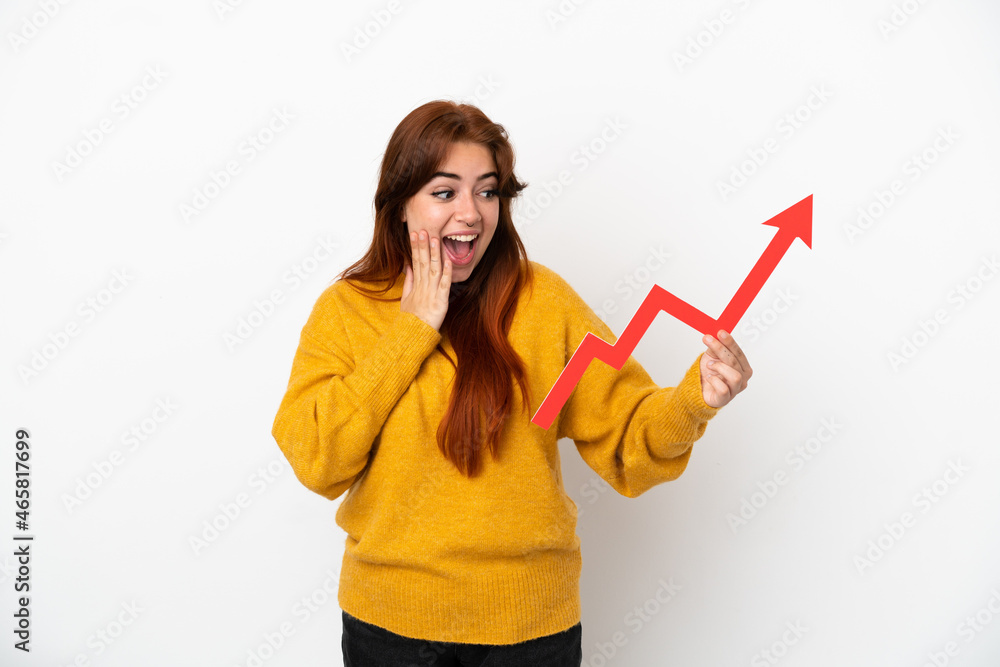 Young redhead woman isolated on white background holding a catching a rising arrow with surprised expression Young redhead woman isolated on white background holding a catching a rising arrow with surprised expression