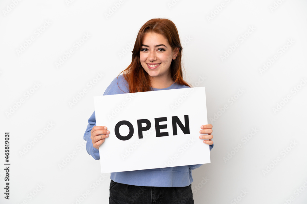 Young redhead woman isolated on white background holding a placard with text OPEN with happy expression Young redhead woman isolated on white background holding a placard with text OPEN with happy expression