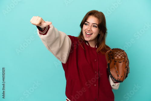 Young redhead woman playing baseball isolated on blue background giving a thumbs up gesture