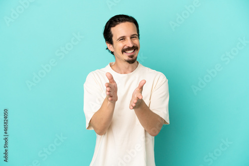 Young caucasian man isolated on blue background applauding after presentation in a conference