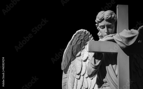Beautiful sad angel with cross. Fragment of an ancient statue with a sweet expression that looks down as symbol of unspeakable sadness and death. Copy space. Horizontal image.