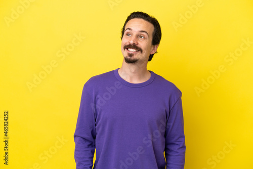 Young caucasian man isolated on yellow background thinking an idea while looking up