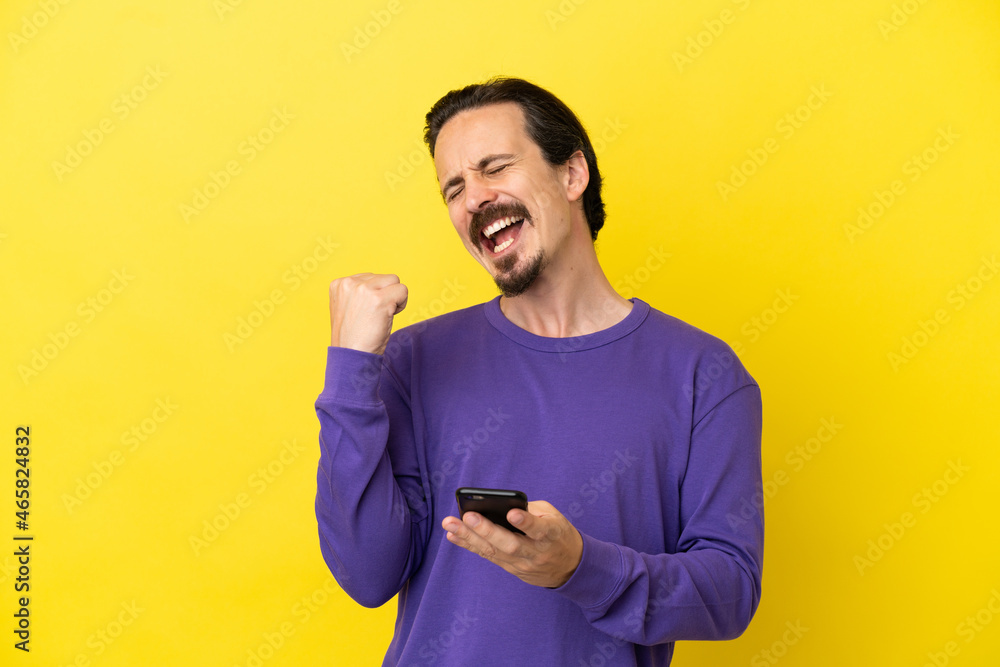 Young caucasian man isolated on yellow background with phone in victory position Young caucasian man isolated on yellow background with phone in victory position