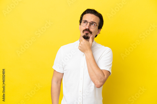 Young caucasian man isolated on yellow background having doubts