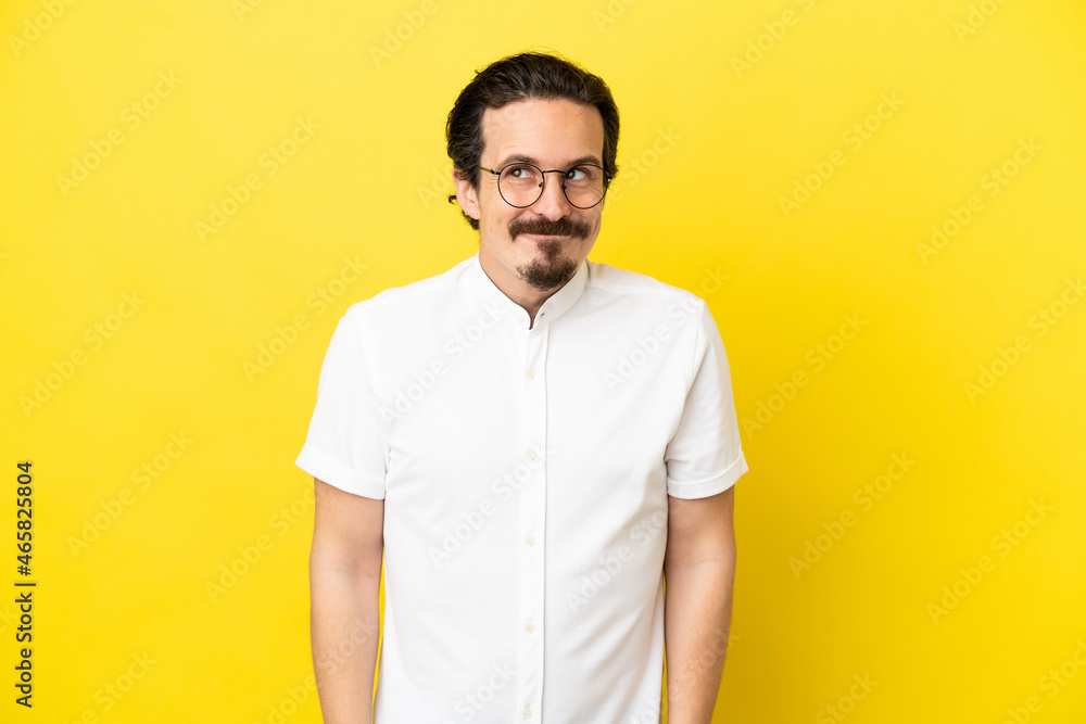 Young caucasian man isolated on yellow background having doubts while looking up Young caucasian man isolated on yellow background having doubts while looking up
