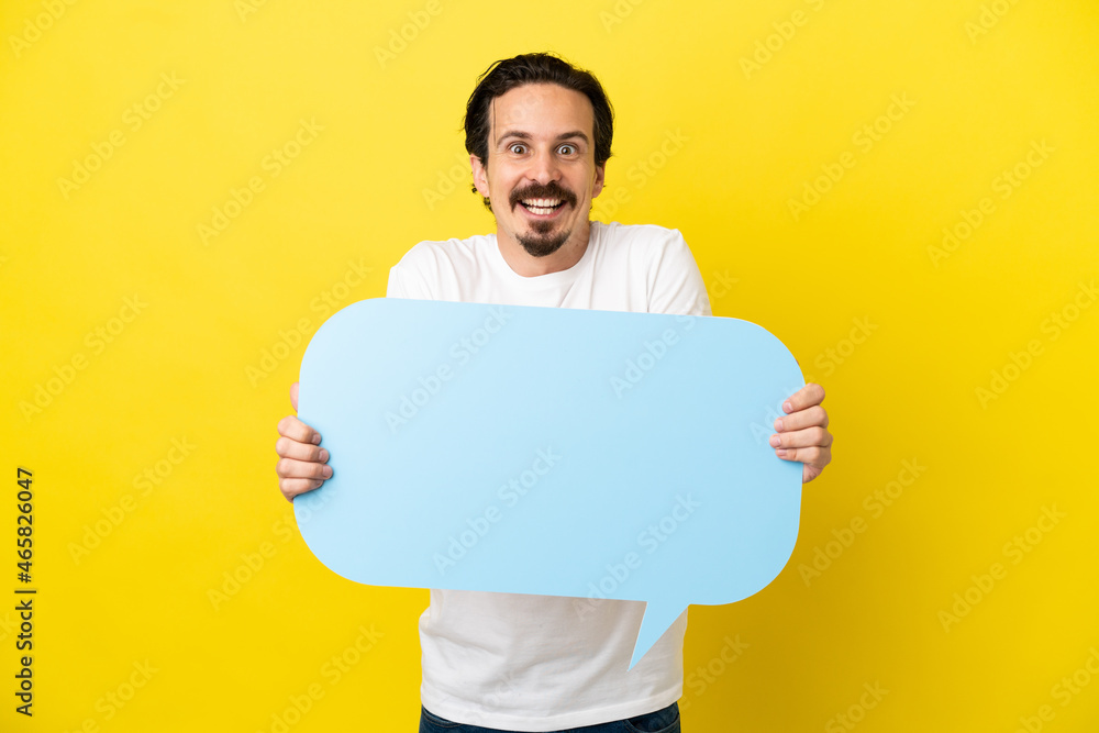 Young caucasian man isolated on yellow background holding an empty speech bubble with surprised expression Young caucasian man isolated on yellow background holding an empty speech bubble with surprised expression