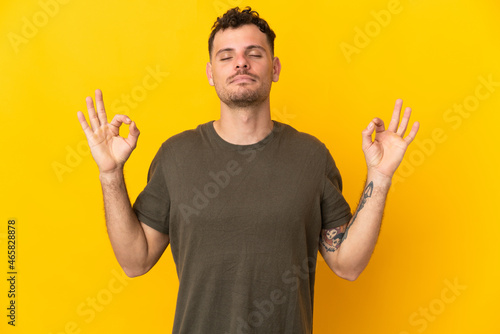 Young caucasian handsome man isolated on yellow background in zen pose