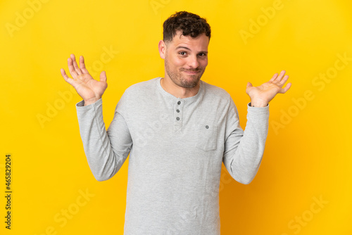 Young caucasian handsome man isolated on yellow background making doubts gesture