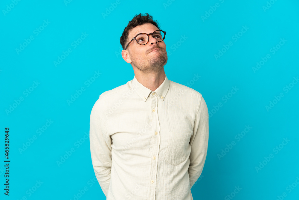 Young caucasian handsome man isolated on blue background and looking up Young caucasian handsome man isolated on blue background and looking up