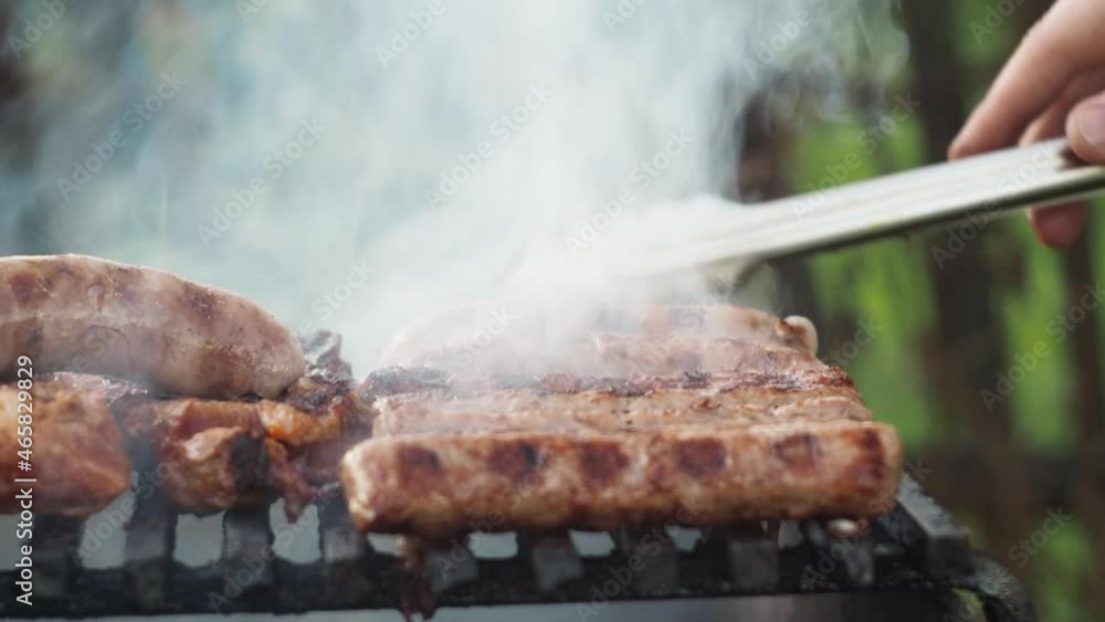 sausages are grilled on coals cooking on a grill. turn it over with tongs. unhealthy and greasy food. smoke from the grill. side view sausages are grilled on coals cooking on a grill. turn it over with tongs. unhealthy and greasy food. smoke from the grill. side view