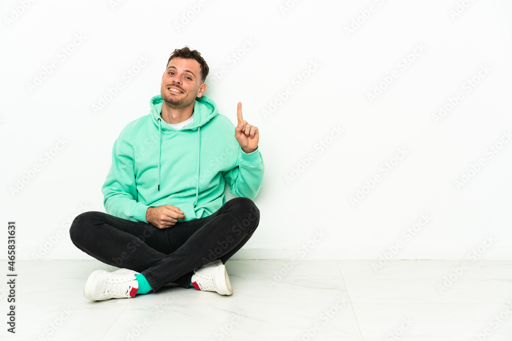 Young handsome caucasian man sitting on the floor pointing with the index finger a great idea Young handsome caucasian man sitting on the floor pointing with the index finger a great idea