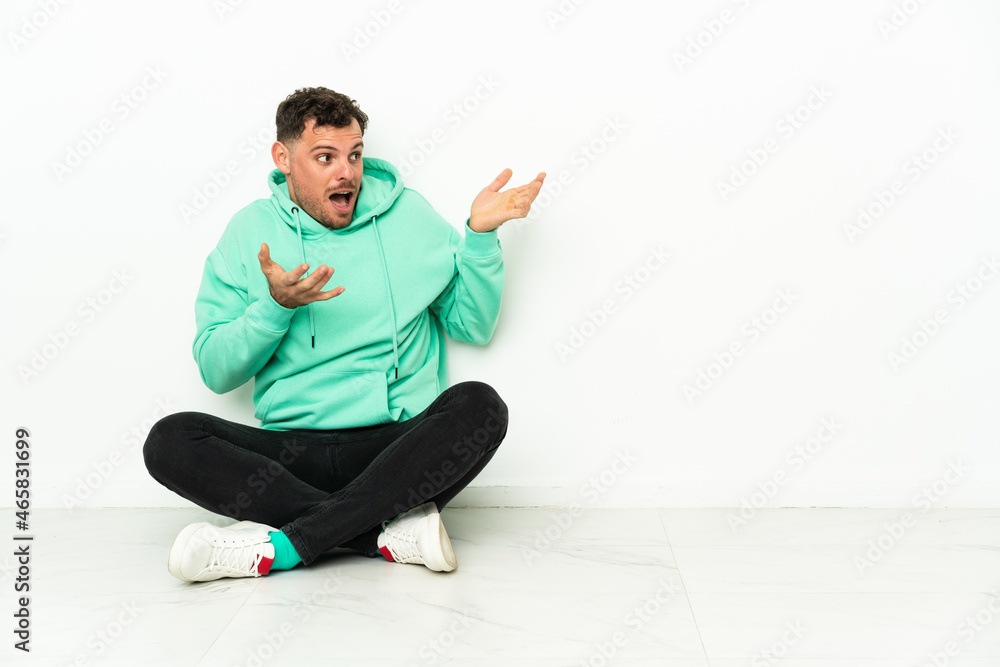 Young handsome caucasian man sitting on the floor with surprise facial expression