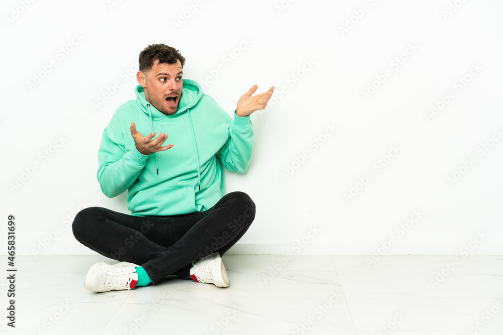 Young handsome caucasian man sitting on the floor with surprise facial expression Young handsome caucasian man sitting on the floor with surprise facial expression